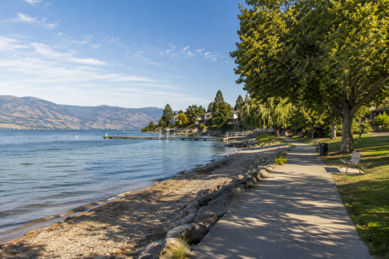 Gellatly waterfront path beside Okanagan Lake, with benches and shade trees.