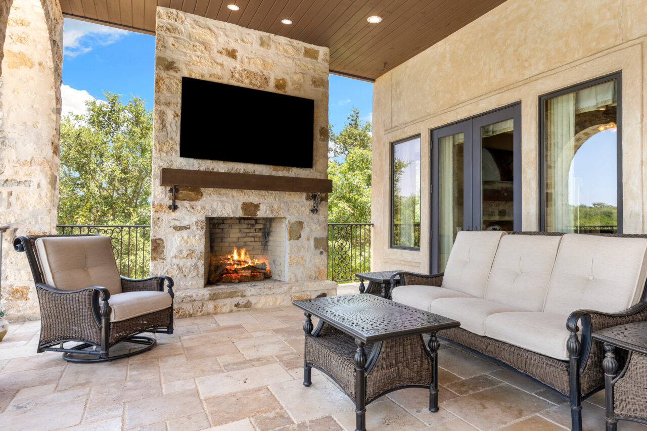 Covered patio with outdoor seating, a stone fireplace, and a wall-mounted television.